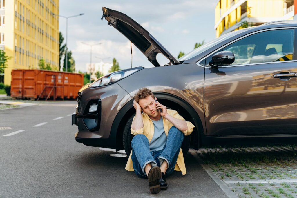 Young man using a mobile phone near a broken car in the city.